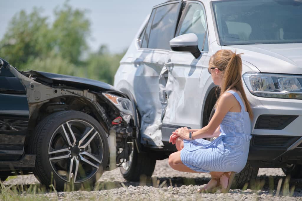 Stressed woman driver sitting on street side shocked after car accident. Road safety and insurance concept